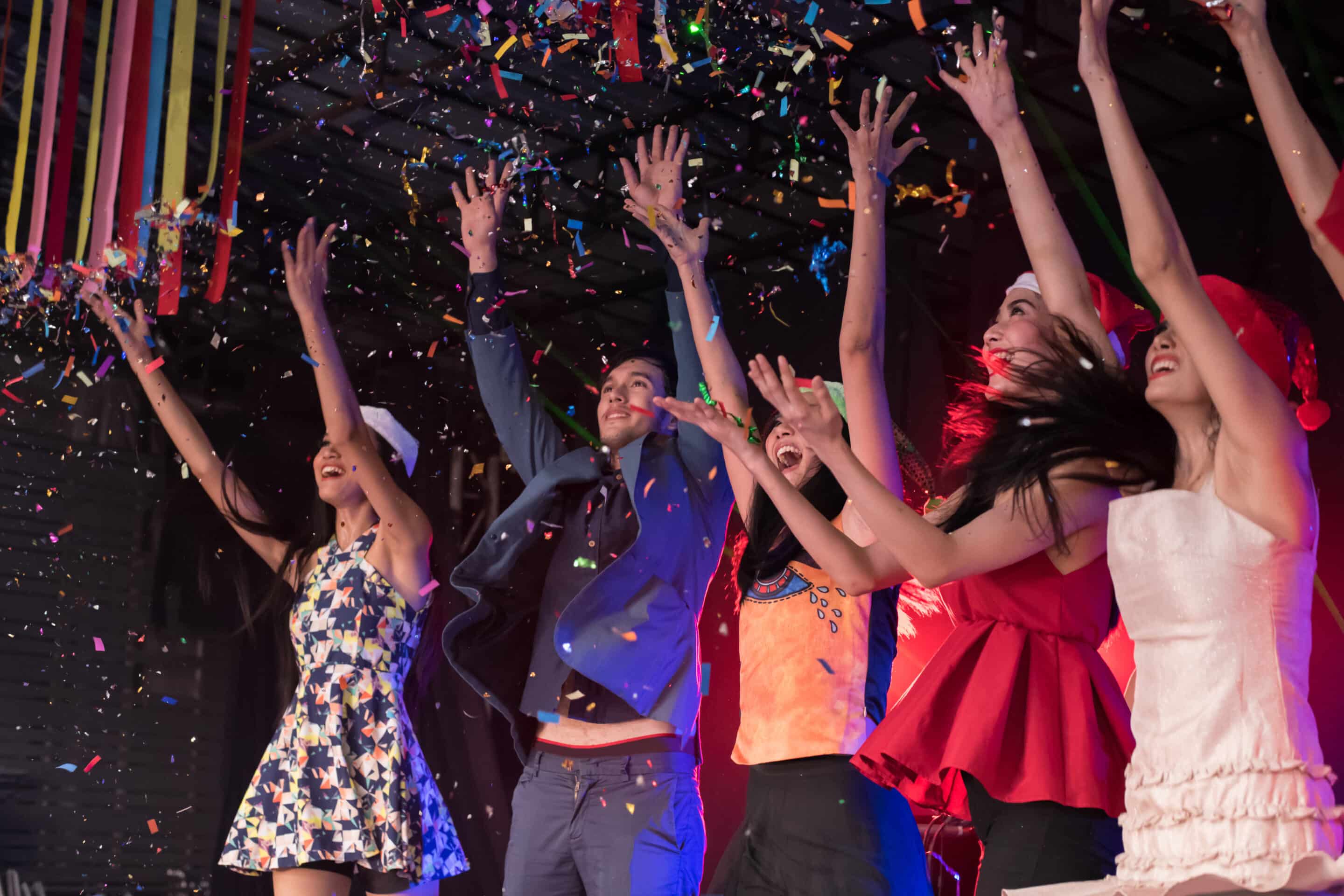 A lively group of people celebrating indoors as colorful confetti falls around them.